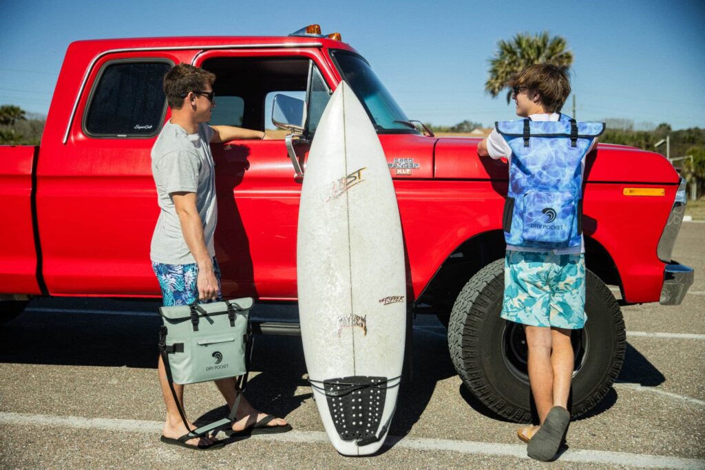 two teens with a surf board and red car