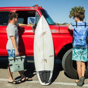 two teens with a surf board and red car